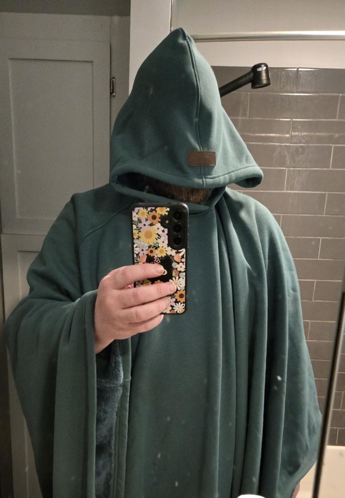 Person wearing a green hooded cloak taking a mirror selfie.